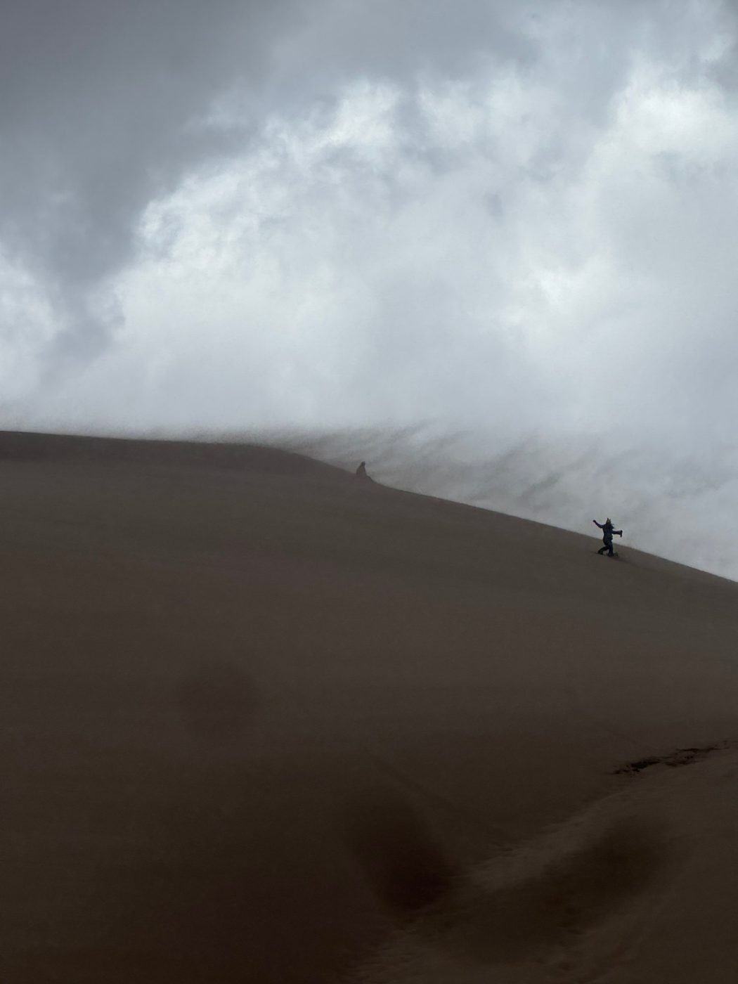 A figure dancing on a sand dune under storm clouds