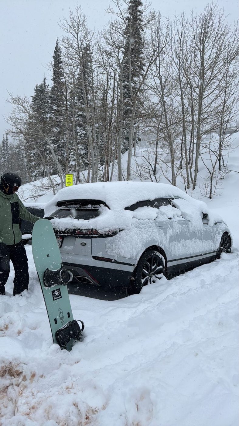 A snowboard next to a snowed-in car