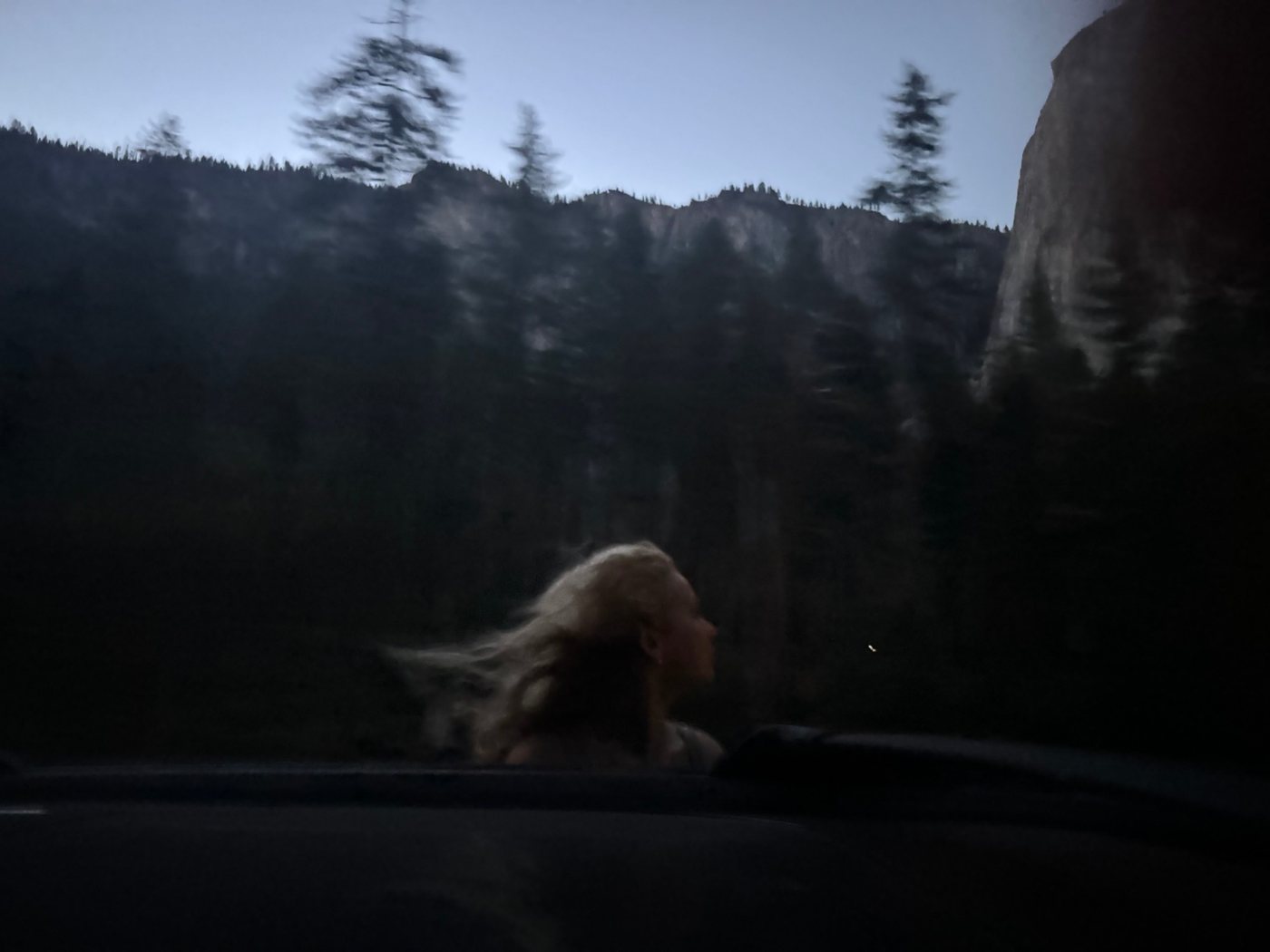 Windblown hair out of a car window at dusk below granite cliffs